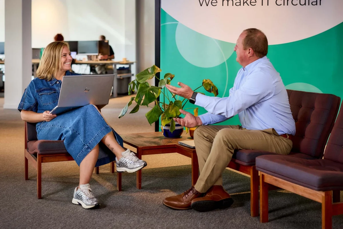 Deux employés de Circular IT Group discutant dans un bureau moderne, avec un ordinateur portable et des plantes en arrière-plan