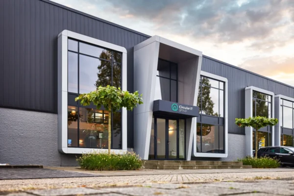 Bâtiment moderne de Circular IT group avec de grandes baies vitrées, une façade grise et un espace végétalisé à l'entrée.