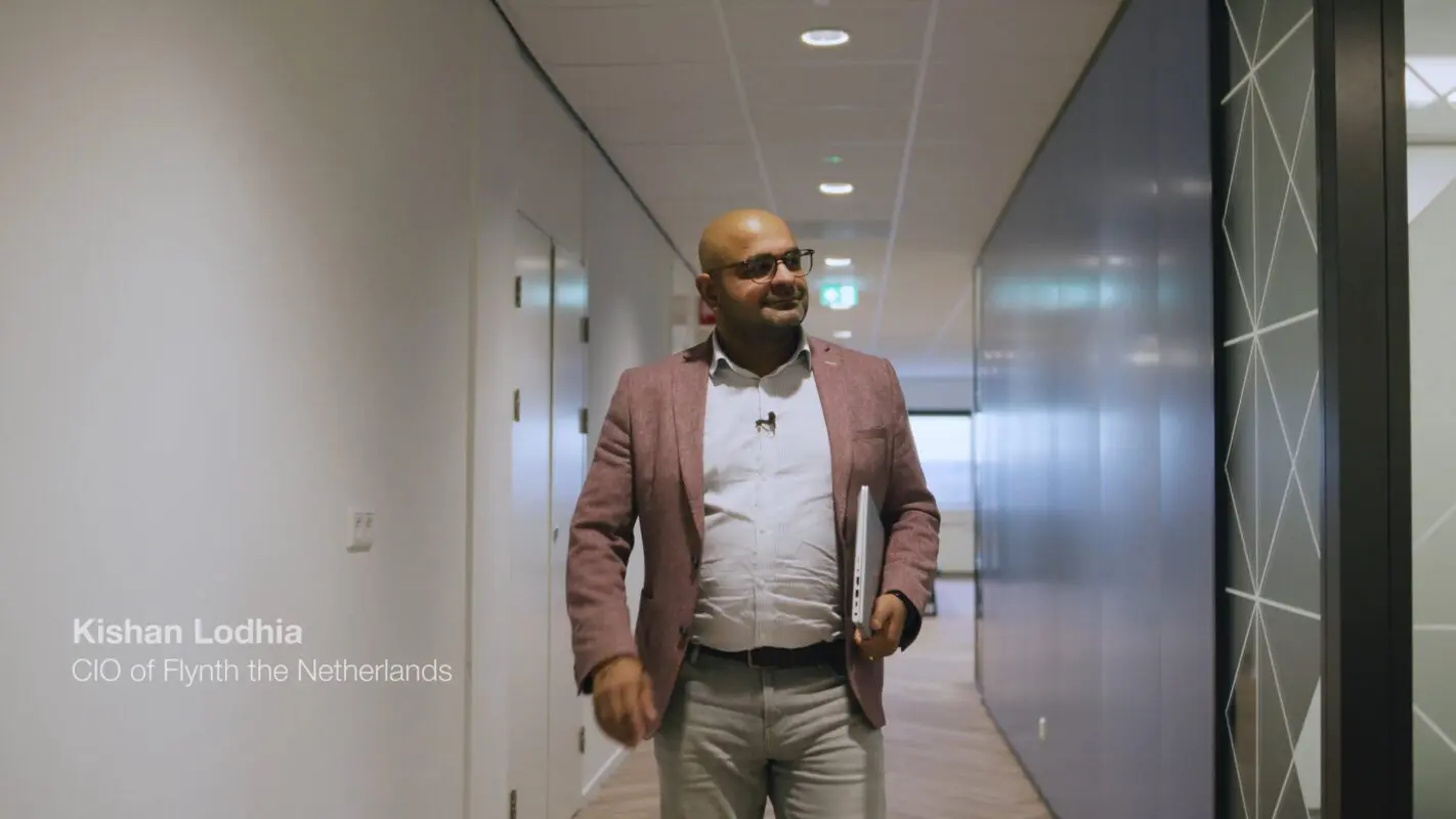 Foto van Kishan Lodhia, CIO van Flynth Nederland, terwijl hij door een kantoorhal loopt met een laptop onder zijn arm. Flynth doneerde IT-apparatuur om positieve maatschappelijke impact te creëren en toegang tot technologie te vergroten.