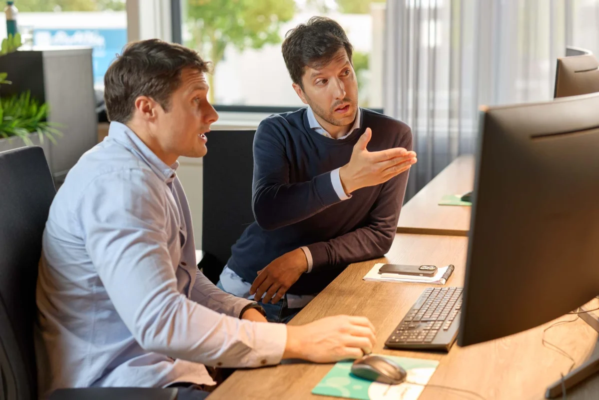Twee collega's bespreken IT hardware oplossingen terwijl ze naar een computerscherm kijken