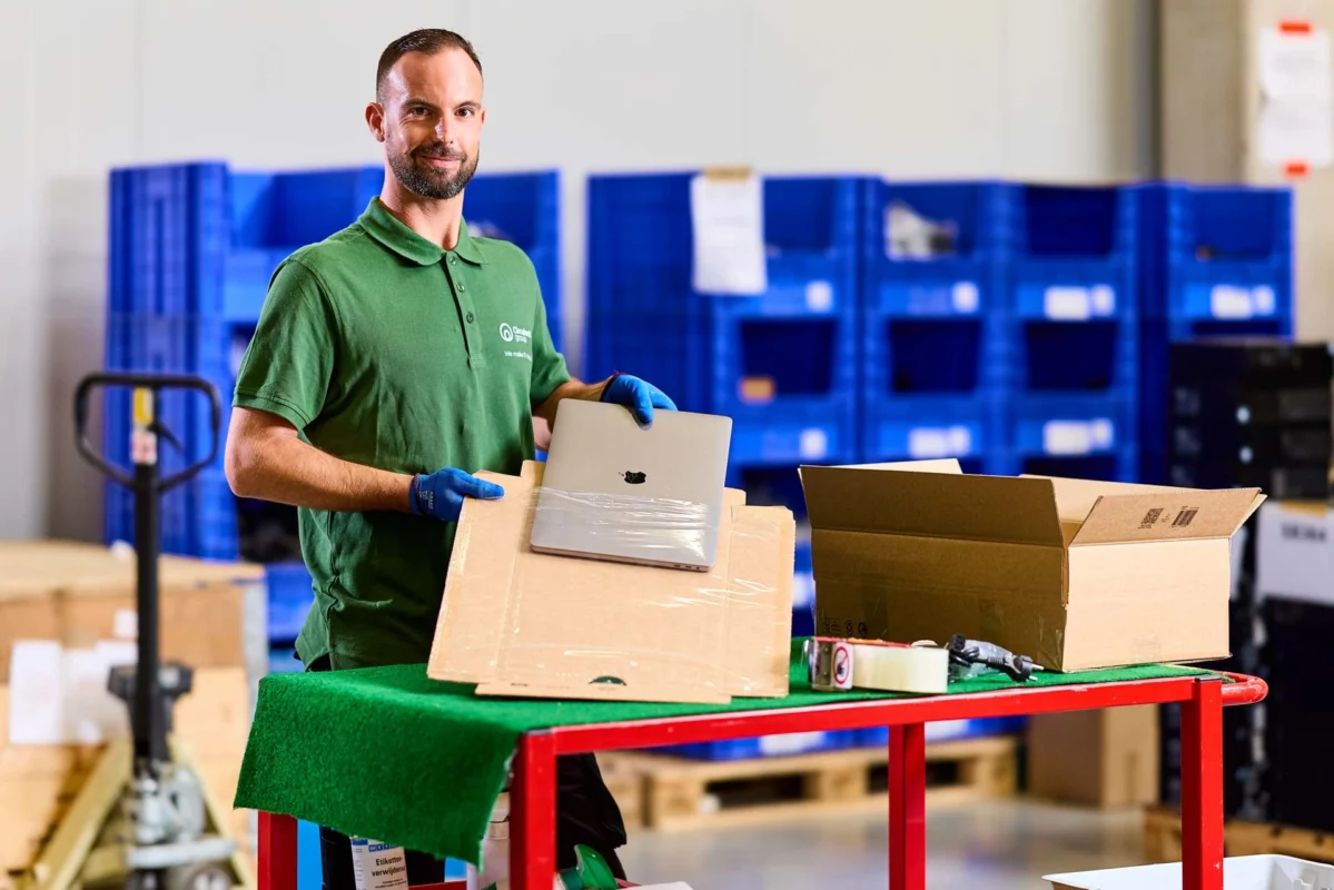 Circular IT group technician prepares a laptop for shipment as part of the Prepare phase of IT lifecycle services—handling imaging, tagging, CMDB registration, and kitting within a sustainable logistics workspace.