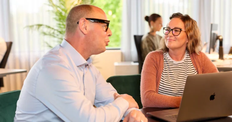 Two colleagues in discussion over a laptop in a bright office, representing how organisations work closely with a strategic ITAD partner to manage secure, circular IT workflows.