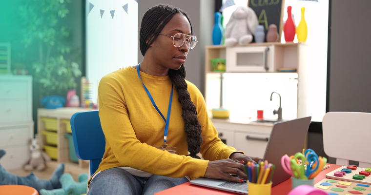 Childcare worker using a refurbished laptop in a daycare setting, demonstrating how refurbished IT for childcare organisations supports daily operations.